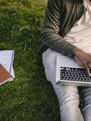 Crop black student with laptop and papers on green lawn
